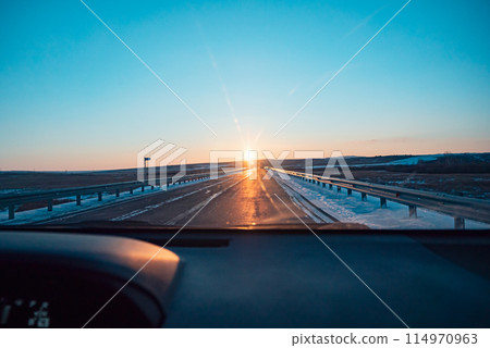 Sunset over a snowy open highway viewed from inside a car 114970963