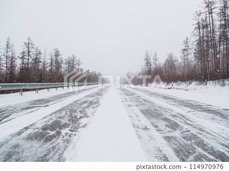 Snow-covered highway surrounded by wintery pine forest on cloudy day Snow-covered highway surrounded by wintery pine forest on cloudy day 114970976