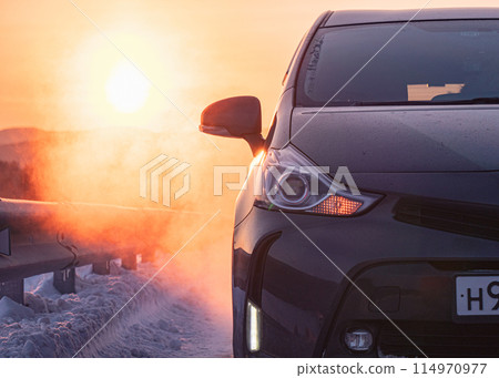 Dark gray car parked on snowy road at sunrise in winter countryside Dark gray car parked on snowy road at sunrise in winter countryside 114970977