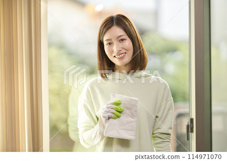 A middle-aged woman wiping windows in the living room A middle-aged woman wiping windows in the living room 114971070