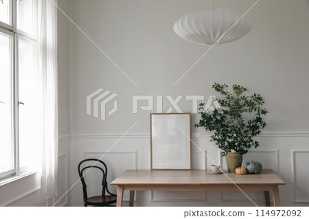 Modern Scandinavian living room interior. Wooden poster, picture frame mockup on office table, Green tree branches in vase, pumpkins, cup of coffee. Vintage chair near window. Stylish home decor. Modern Scandinavian living room interior. Wooden poster, picture frame mockup on office table, Green tree branches in vase, pumpkins, cup of coffee. Vintage chair near window. Stylish home decor. 114972092