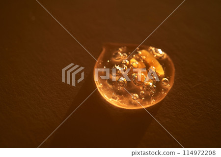 Drop of serum shimmering in the sun on a beige background. 114972208
