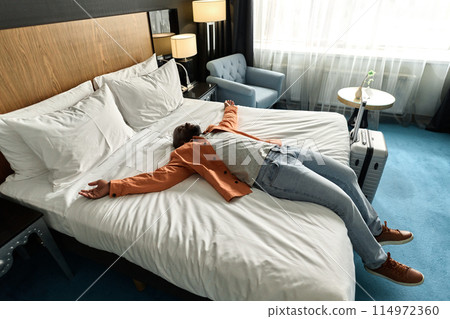 High angle view at exhausted African American man lying on bed in hotel room after long travel copy space 114972360