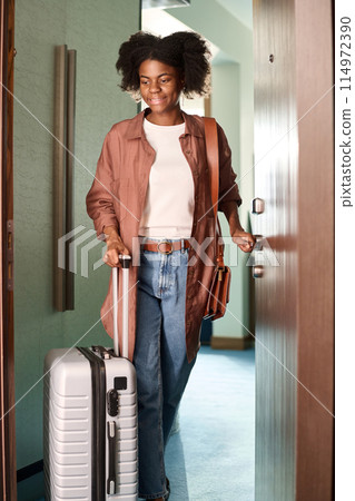 Vertical full length portrait of young Black woman opening door to hotel room and arriving at resort while travelling 114972390