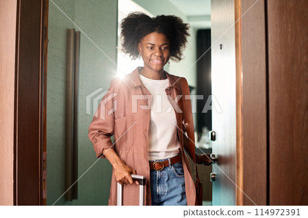 Waist up portrait of smiling African American woman entering hotel room with suitcase copy space 114972391