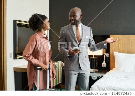 Portrait of luxury hotel manager welcoming young Black woman entering hotel room enjoying travel copy space Portrait of luxury hotel manager welcoming young Black woman entering hotel room enjoying travel copy space 114972425
