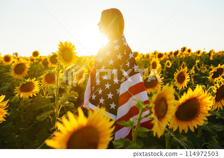 Beautiful girl with the American flag in a sunflower field. 4th of July. Fourth of July. Freedom. 114972503