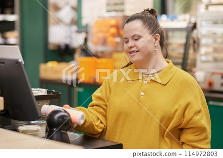 Waist up portrait of smiling young woman with Down syndrome using self checkout machine while buying groceries in supermarket copy space Waist up portrait of smiling young woman with Down syndrome using self checkout machine while buying groceries in supermarket copy space 114972803