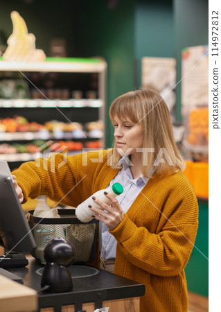 Vertical portrait of blonde adult woman using self checkout machine in supermarket and buying groceries Vertical portrait of blonde adult woman using self checkout machine in supermarket and buying groceries 114972812