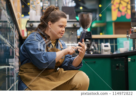 Side view portrait of independent young woman with Down syndrome working in cafe and using smartphone during break copy space 114972822