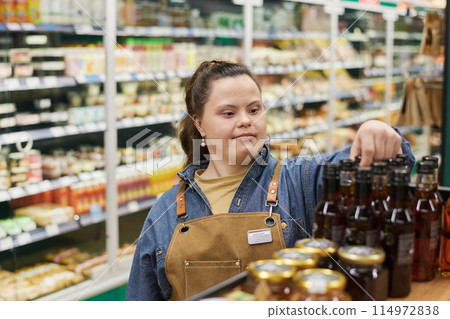 Waist up portrait of adult woman with Down syndrome working in supermarket and reviewing shelf stock Waist up portrait of adult woman with Down syndrome working in supermarket and reviewing shelf stock 114972838