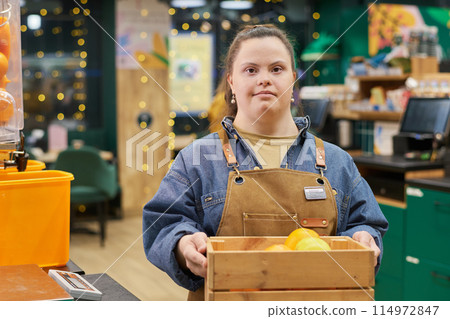 Waist up portrait of young woman with disability working in supermarket and looking at camera holding box with fresh fruits copy space 114972847