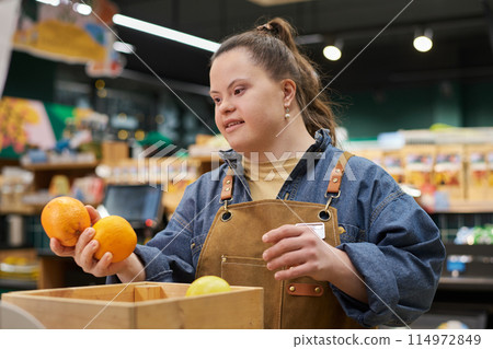 Waist up portrait of smiling young woman with disability working in supermarket sorting fresh fruits and produce 114972849