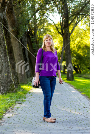 Blonde woman standing in the park. Middle-aged elegance woman enjoying summer day. enhancing lifestyle and wellness concept. Woman 40 years old 114972939