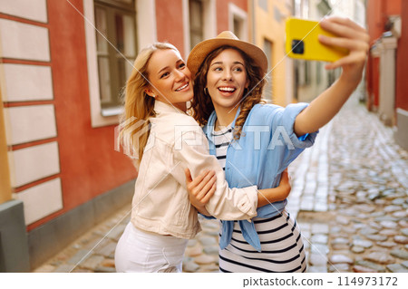 Young women taking selfies on sunny day while walking along European streets. Concept of tourism. 114973172