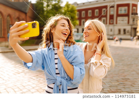 Happy women taking selfie while walking down street. Fashion, travel, technology, blogging concept. 114973181