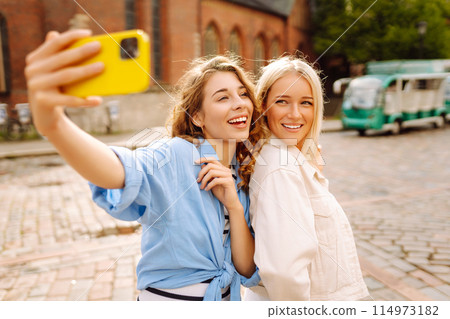 Happy women taking selfie while walking down street. Fashion, travel, technology, blogging concept. 114973182