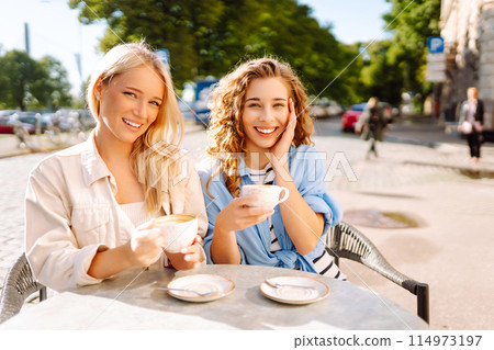 Portrait of a smiling young women friends sitting outdoors in cafe drinking coffee. Beauty, relax. Portrait of a smiling young women friends sitting outdoors in cafe drinking coffee. Beauty, relax. 114973197
