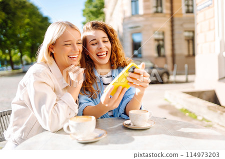 Two young women sitting in the cafe. Coffee break after shopping. Blogging, tourism. 114973203