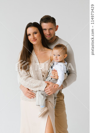 Happy family of three, a man, a woman and a baby, are passing for a picture in the studio on a white background Happy family of three, a man, a woman and a baby, are passing for a picture in the studio on a white background 114973429