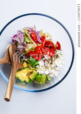 Feta and avocado salad with tomatoes and red onions in glass bowl, white background. 114974071