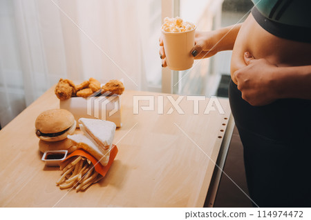 To eat or not. Cheerless plump woman looking at the burger while thinking to eat it or not To eat or not. Cheerless plump woman looking at the burger while thinking to eat it or not 114974472