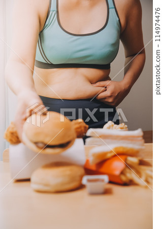 To eat or not. Cheerless plump woman looking at the burger while thinking to eat it or not To eat or not. Cheerless plump woman looking at the burger while thinking to eat it or not 114974476