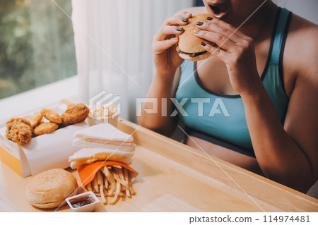 Binge eating disorder concept with woman eating fast food burger, fired chicken , donuts and desserts Binge eating disorder concept with woman eating fast food burger, fired chicken , donuts and desserts 114974481