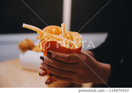 Asian woman holding french fries and eating happily in restaurant Asian woman holding french fries and eating happily in restaurant 114974507