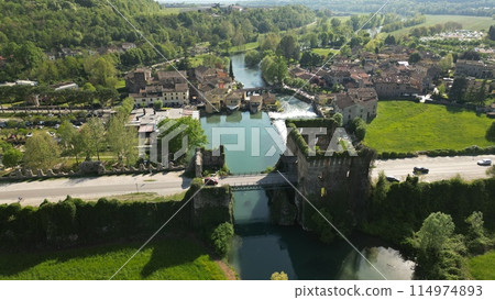 Beautiful panoramic aerial view of the mill village of Borghetto sul Mincio in the south of Lake Garda, in Veneto, Italy. Drone footage of the small medieval village. Beautiful panoramic aerial view of the mill village of Borghetto sul Mincio in the south of Lake Garda, in Veneto, Italy. Drone footage of the small medieval village. 114974893
