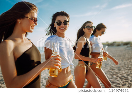 Four beautiful girls cheers and drink beers on the beach, enjoying vacation. Vacation time laughing and smiling. 114974951