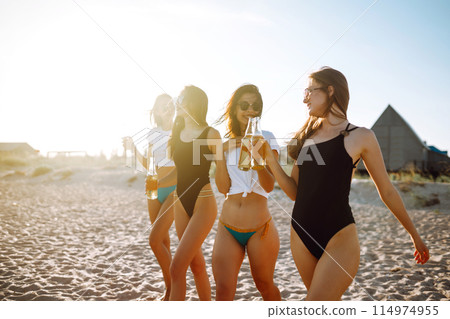 Four beautiful girls cheers and drink beers on the beach, enjoying vacation. Vacation time laughing and smiling. 114974955