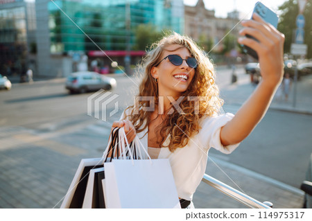 Beautiful woman with shopping bags makes selfie. Young woman walking shopping. Lifestyle concept. Beautiful woman with shopping bags makes selfie. Young woman walking shopping. Lifestyle concept. 114975317