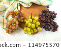 Cutting board with bunch of organic green, pink and blue grapes on white wooden background.. 114975570