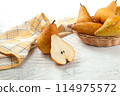 Whole and halves of pears, wicker basket and yellow kitchen towel on white wooden background.. 114975572
