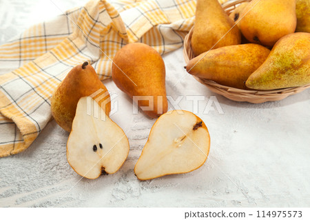 Whole and halves of pears, wicker basket and yellow kitchen towel on white wooden background.. Whole and halves of pears, wicker basket and yellow kitchen towel on white wooden background.. 114975573