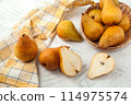 Whole and halves of pears, wicker basket and yellow kitchen towel on white wooden background.. 114975574