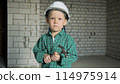 a boy in a helmet and with a hammer is standing on a construction site 114975914