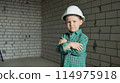 A cute little boy stands on a construction site and looks at the camera 114975918