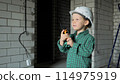 A small boy is standing on a construction site and talking on a walkie-talkie 114975919