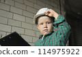 A boy at a construction site holds his helmet and looks into the camera 114975922