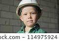 A portrait of a boy in a white helmet and a green shirt at a construction site. 114975924