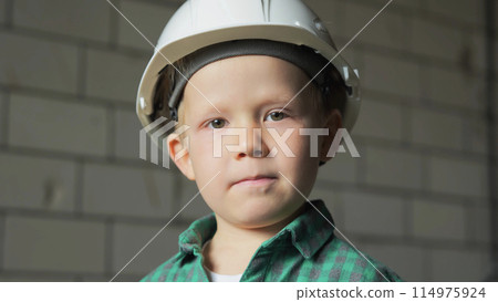 A portrait of a boy in a white helmet and a green shirt at a construction site. 114975924