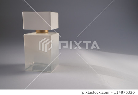 A white perfume bottle is placed on a white surface in the room 114976320