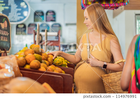 A pregnant woman is at a fruit stand in a grocery store Pregnant woman buying organic vegetables and fruits at Mexican style farmers market 114976991