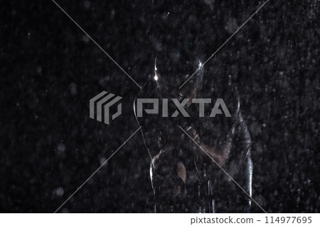 A triathlete braving the rain as he cycles through the night, preparing himself for the upcoming marathon. The blurred raindrops in the foreground and the dark, moody atmosphere in the background add 114977695