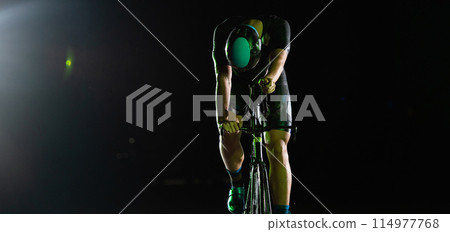 A triathlete rides his bike in the darkness of night, pushing himself to prepare for a marathon. The contrast between the darkness and the light of his bike creates a sense of drama and highlights the 114977768