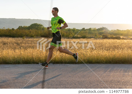 Triathlete in professional gear running early in the morning, preparing for a marathon, dedication to sport and readiness to take on the challenges of a marathon. Triathlete in professional gear running early in the morning, preparing for a marathon, dedication to sport and readiness to take on the challenges of a marathon. 114977786