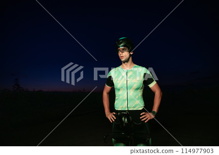 A triathlete resting on the road after a tough bike ride in the dark night, leaning on his bike in complete exhaustion A triathlete resting on the road after a tough bike ride in the dark night, leaning on his bike in complete exhaustion 114977903