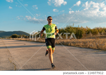 Triathlete in professional gear running early in the morning, preparing for a marathon, dedication to sport and readiness to take on the challenges of a marathon. Triathlete in professional gear running early in the morning, preparing for a marathon, dedication to sport and readiness to take on the challenges of a marathon. 114977912